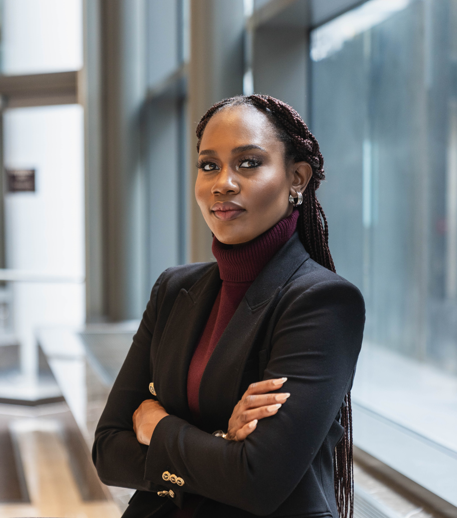 Woman wearing black blazer with gold buttons standing with head in profile in a glazed reception area